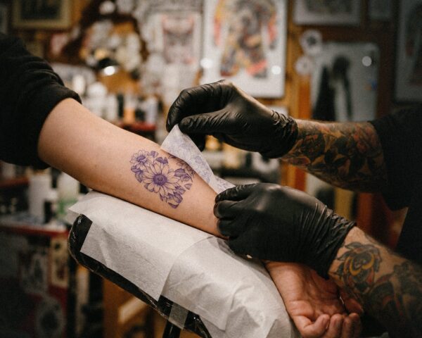 A tattoo artist wipes a fresh flower tattoo on a client's forearm