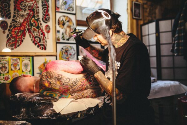 A tattoo artist tattoos a Japanese-style piece on a client's back and side