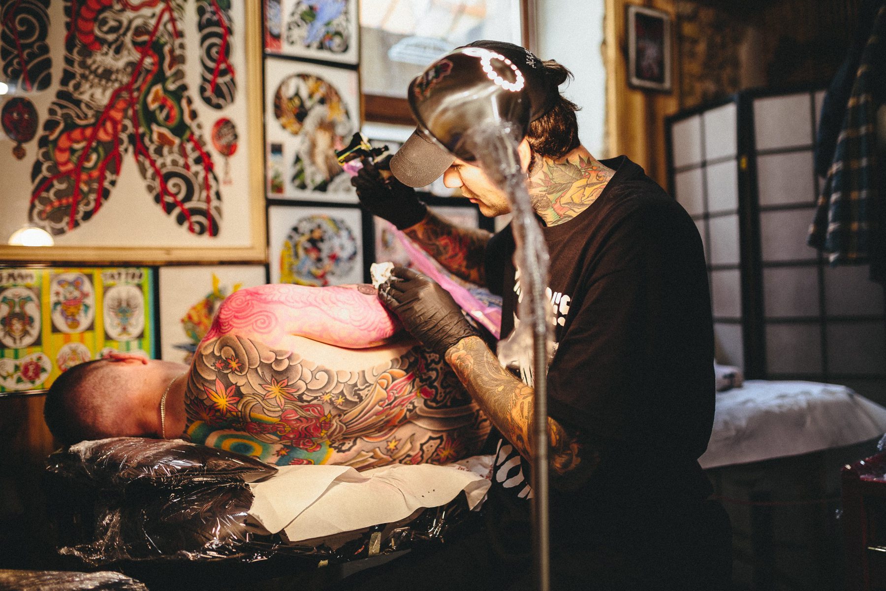 A tattoo artist tattoos a Japanese-style piece on a client's back and side