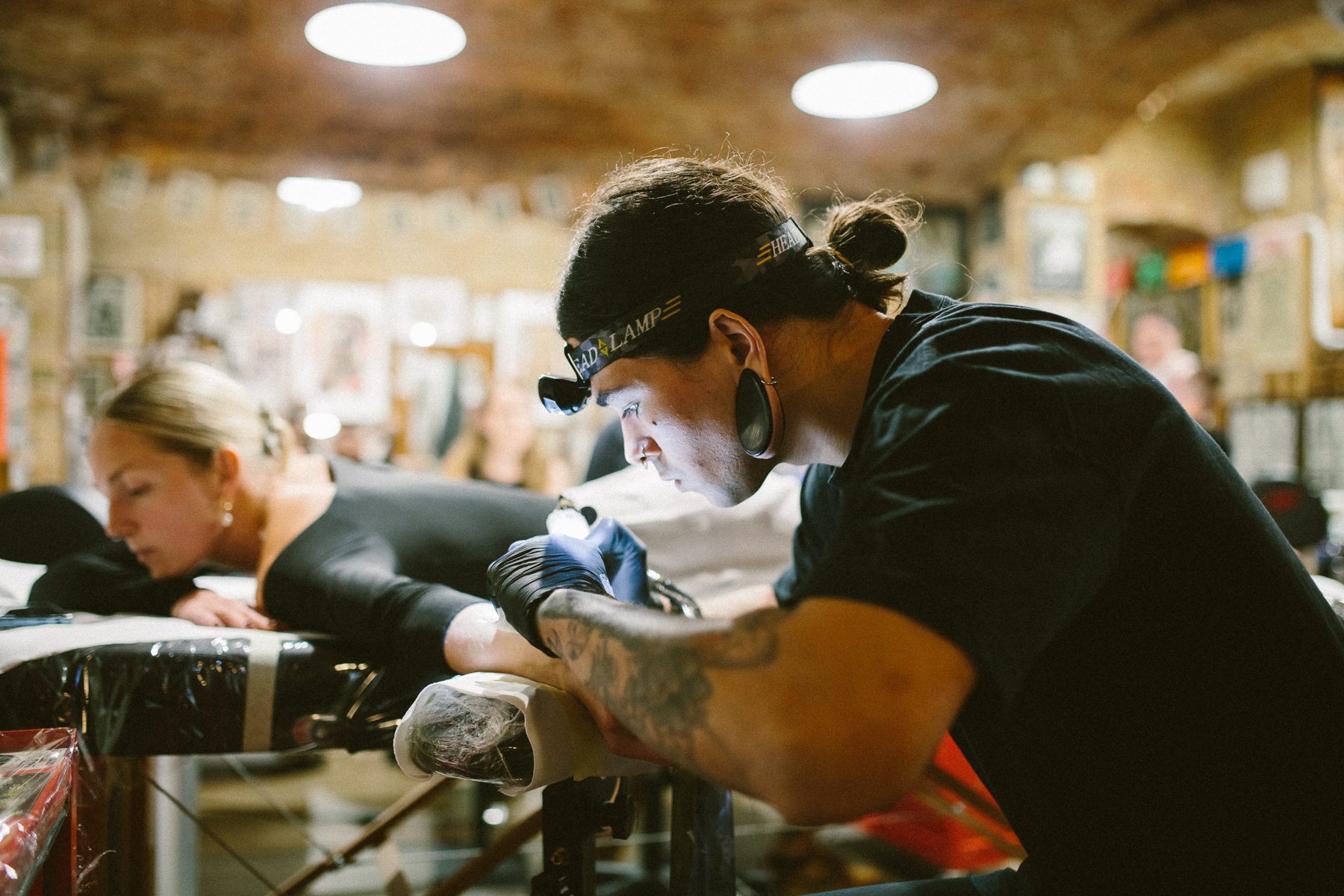A tattoo artist in a face mask tattoos a woman lying on the bench