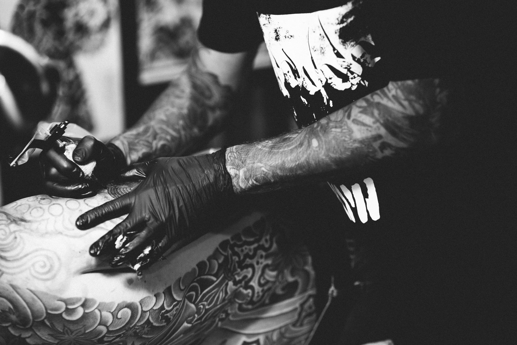 Black and white close-up of a tattoo artist working on a large back piece