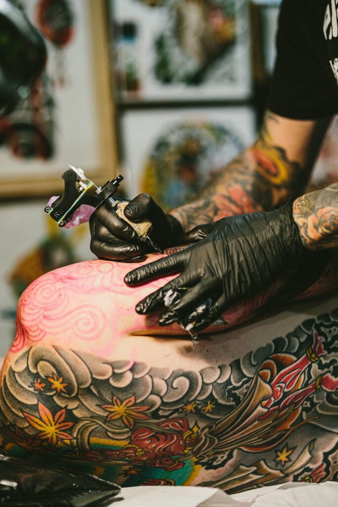 Close-up of a tattoo machine and gloved hands on a colour back piece