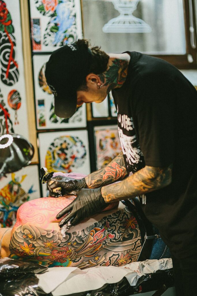 A tattoo artist works on a large colour Japanese-style back piece
