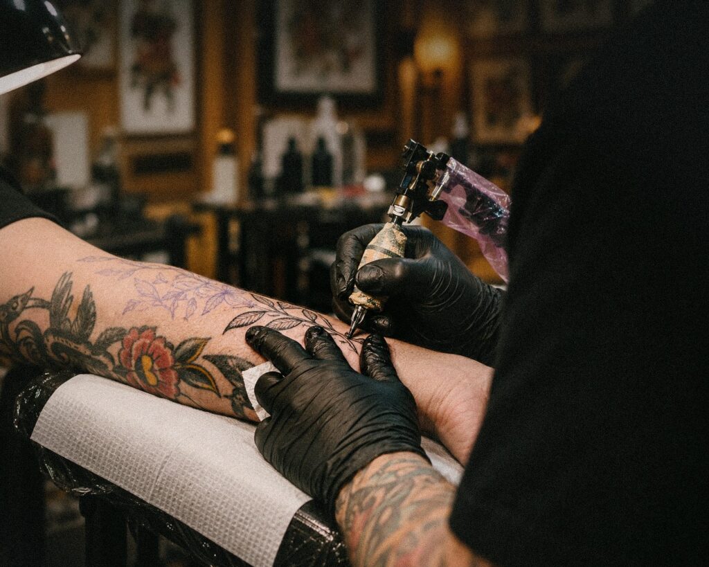 A tattoo artist in gloves tattoos flowers on a client's forearm